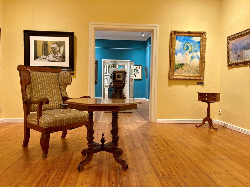 Musemsraum mit Holzboden, gelben Wänden und Kunstwerken an der Wand